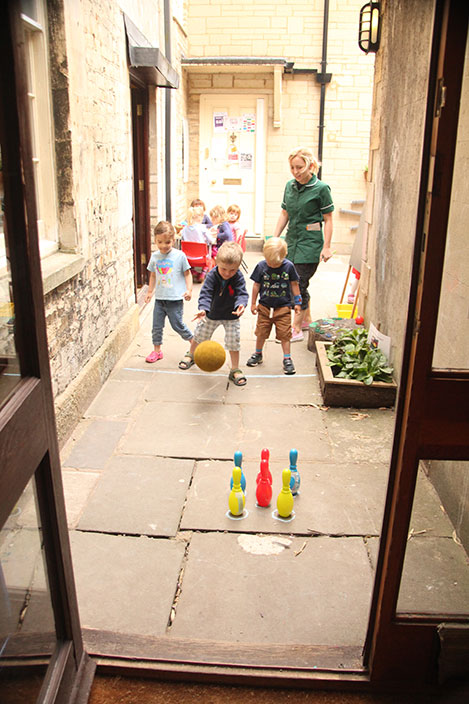 Playing skittles in the pre-school courtyard classroom at Acorns Nursery School, Cirencester.